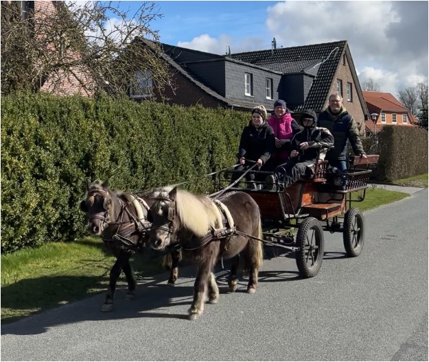 Mehrere Personen auf einer Kutschfahrt durch den Ort.